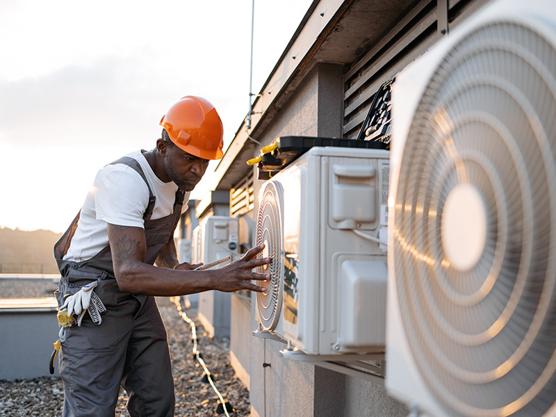 HVAC contractor in hard hat performing outdoor AC installation and system checks on commercial ductless condenser units
