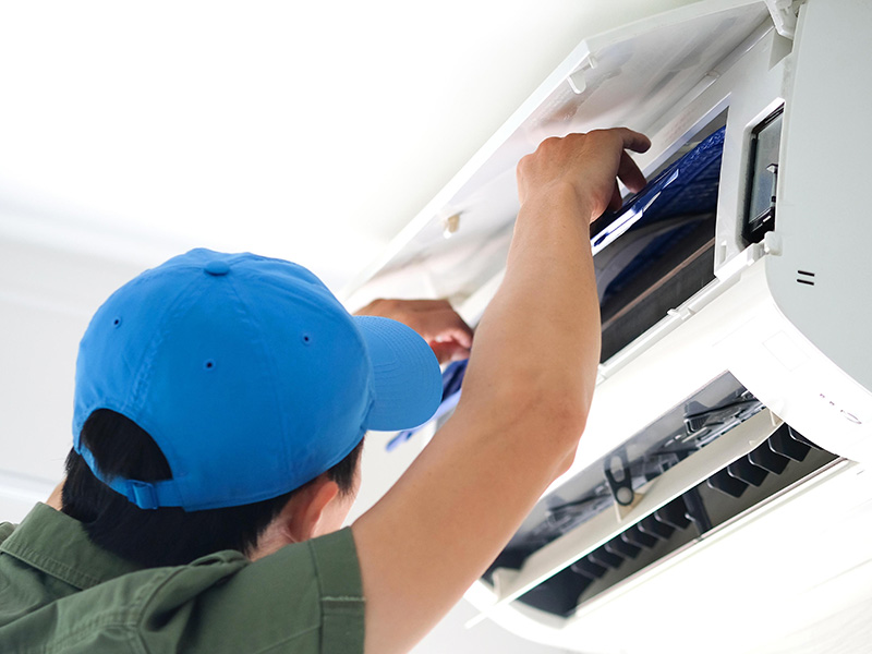 HVAC technician performing indoor AC repair and air filter replacement on a ductless mini-split unit