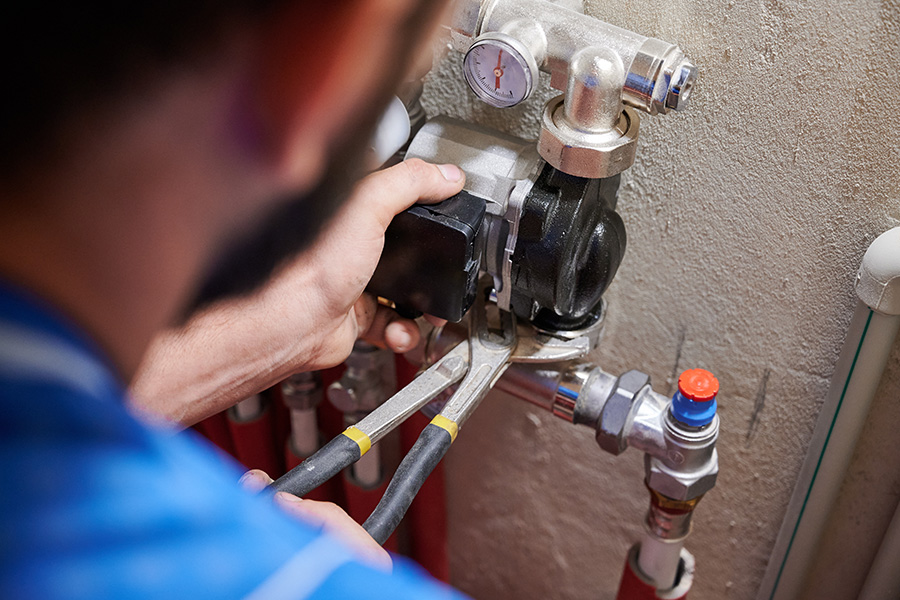 Professional technician performing residential plumbing repair on a water heating pump system with wrench in Livonia, MI