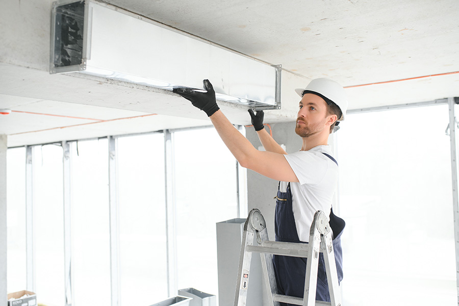 Airtech technician performing routine commercial HVAC maintenance on ceiling ventilation