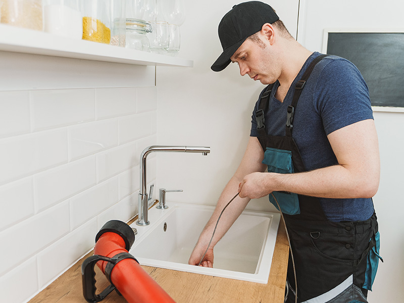Airtech Mechanical plumber using an auger snake tool for kitchen sink drain cleaning in Livonia, MI