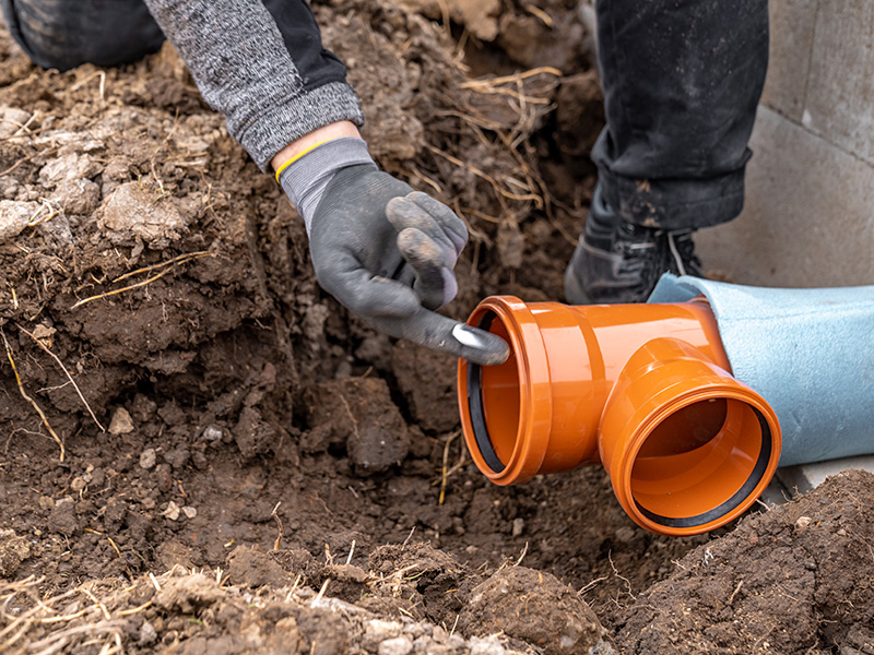 Plumber applying lubricant to a PVC pipe fitting during sewer line repair in Livonia, MI
